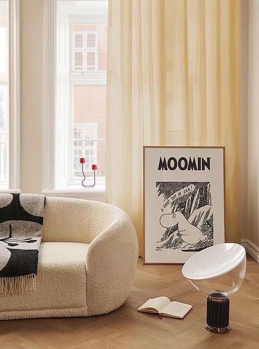 Framed Moomin poster leaning against the wall of a bright, bouclé-furnished lounge — playful licensed art prints that bring personality to business and hospitality spaces