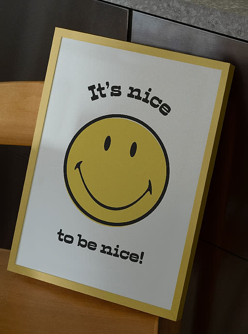 Smiley "It's nice to be nice" poster in a gold frame resting on a wooden chair — bold, characterful wall art for cafés, offices and other commercial spaces