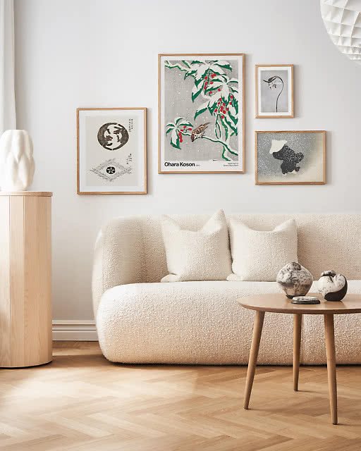 A four-print gallery wall of Japanese-style botanical and bird illustrations by Ohara Koson, featuring delicate depictions of sparrows, foliage and snow, displayed above a rounded cream boucle sofa.