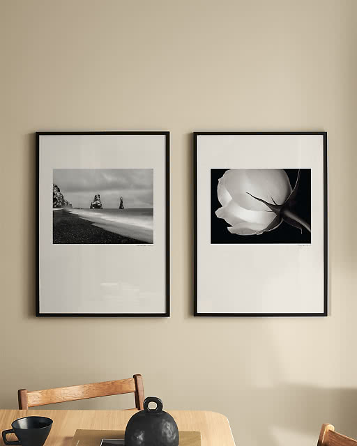 Two black and white photographic prints — one of a misty seascape and one of a close-up still life — displayed in black frames above a wooden dining table.