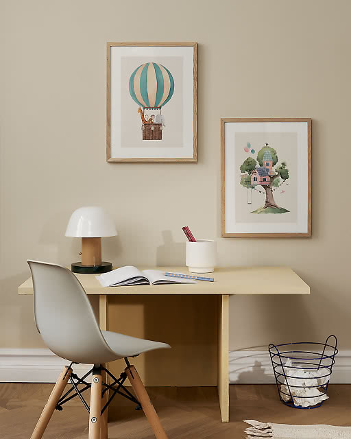 Two children's watercolour prints above a yellow desk — a hot air balloon with animals and a whimsical treehouse illustration.