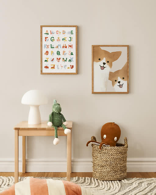 An animal alphabet poster and a cute corgi illustration displayed in a soft children's room with stuffed toys and a wicker basket.