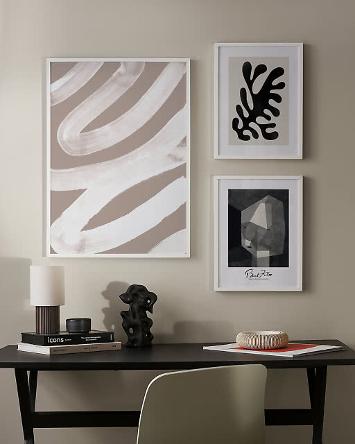 A large white brushstroke print, a black Matisse leaf cutout, and a Paul Klee print above a dark desk with sculptural objects.