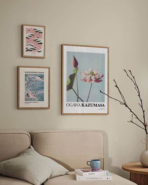 Three Japanese prints — pink cloud scene, Manchurian Crane, and an Ogawa Kazumasa lotus flower — above a neutral sofa.