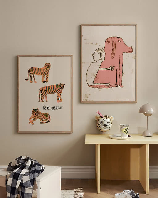 A Roaar tiger print and a quirky pink dog illustration displayed above a yellow side table in a children's room.