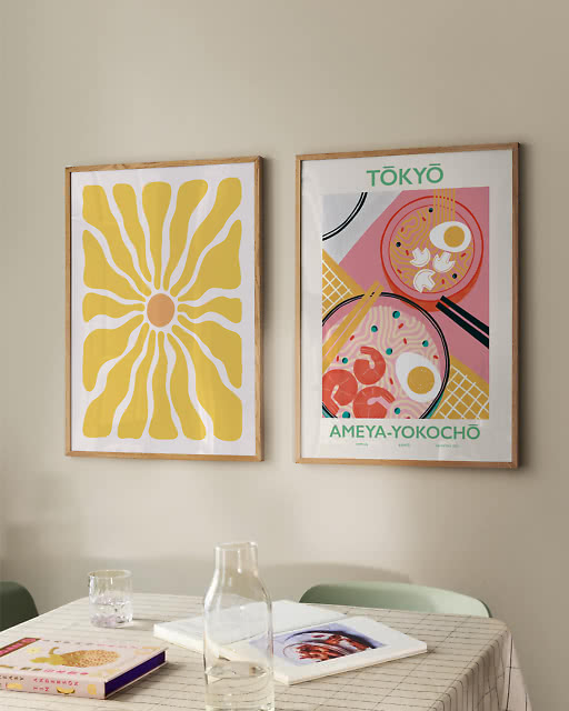A yellow sunburst print and a colourful Tokyo Ameya-Yokochō ramen print above a grid-cloth dining table.