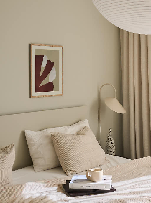 Framed abstract cut-out print above a bed dressed in soft linen — understated, refined art prints that add a calm, premium feel to hotel rooms