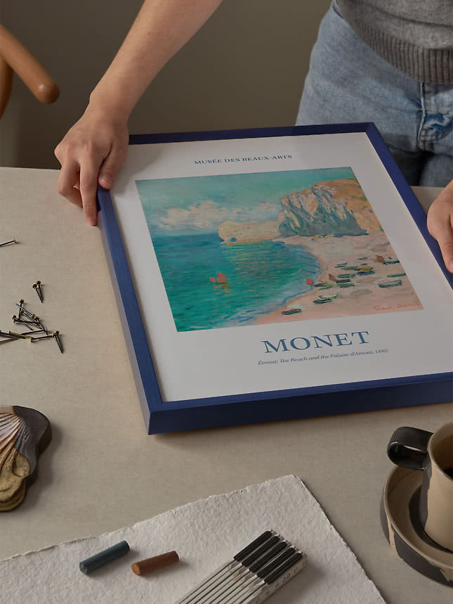 Mains plaçant une affiche de Monet dans un cadre bleu sur une table de travail