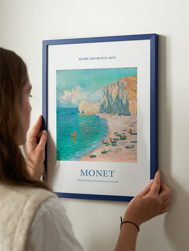 Femme accrochant au mur une affiche de Monet dans un cadre bleu
