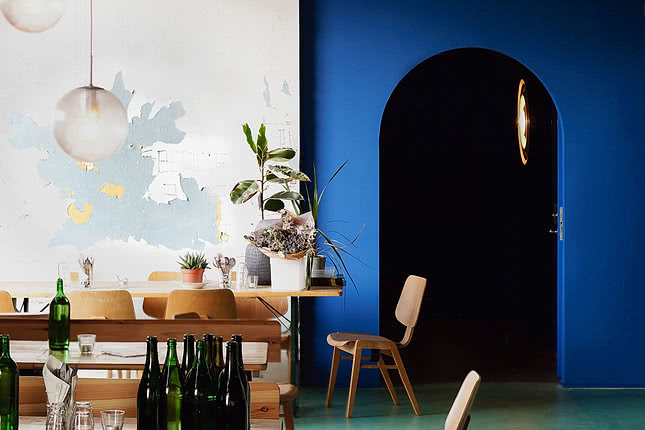 Restaurant avec de longues tables en bois, des bouteilles de vin et un mur bleu profond