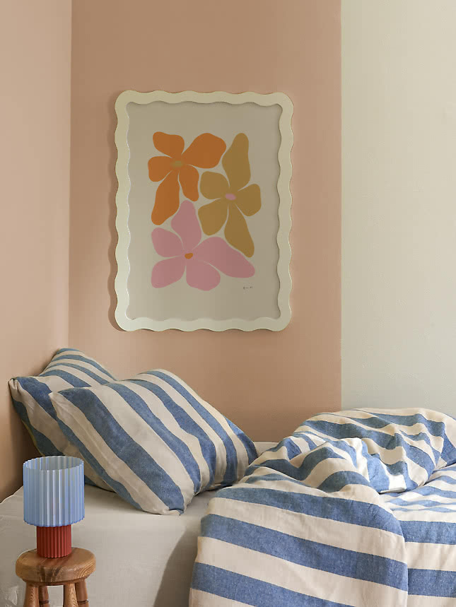 Bloemenprint in een crèmekleurige Wavy Frame boven een bed met gestreept beddengoed