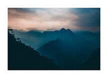 Siluetas de montañas brumosas al atardecer bajo un cielo dramático