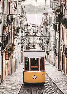 Yellow tram on a steep cobblestone street between narrow buildings and overhead wires