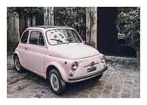 Light pink vintage car parked on a cobblestone courtyard in front of a leafy building