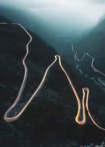 Winding mountain road at dusk with light trails through a misty valley
