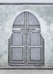 Ornate double door with geometric patterns set in a white arched wall