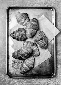 Cinque croissant su carta da forno su una teglia di metallo, vista dall'alto