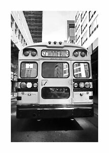 Photo en noir et blanc de l’arrière d’un bus scolaire entre de hauts immeubles