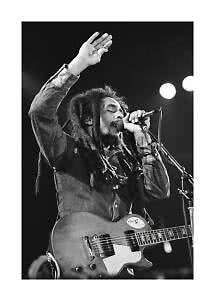 Sort-hvidt foto af sanger med dreadlocks og guitar på scenen, synger i mikrofon med hånden løftet