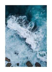 Aerial view of crashing waves with white foam in turquoise sea above rocks