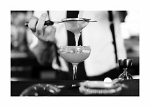 Gros plan en noir et blanc d’un barman filtrant un cocktail dans un verre à pied.