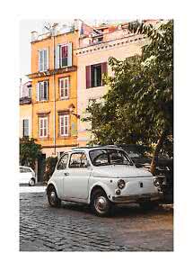 White vintage car parked on a cobblestone street beside warm-toned buildings and trees