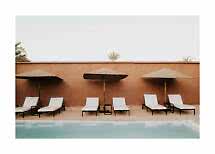Sun loungers with white cushions and straw parasols by a pool against a terracotta wall