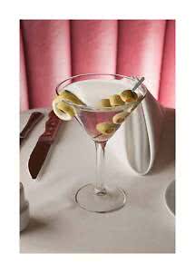 Martiniglas met heldere cocktail, groene olijven en citroenschil op een gedekte tafel met roze achtergrond