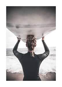 Vue de dos d’une personne en combinaison noire tenant une planche de surf sur la plage