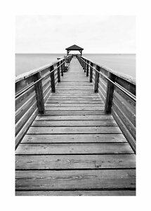 Black and white photo of a long wooden pier with railings leading to a small gazebo over the water