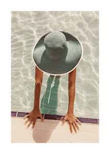 Top view of person in pool wearing a large gray sun hat, hands on pool edge