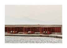 Cabañas de madera con tumbonas junto a una piscina, frente a una pared con persianas y montañas