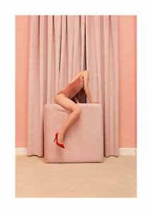Modella in body rosa e tacchi rossi piegata su un cubo rosa davanti a tende