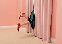 Jambes en escarpins rouges et jupe verte dépassant derrière des rideaux roses dans une pièce rose