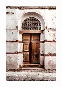 Old wooden door in an arched doorway with wrought iron grille on a weathered white wall