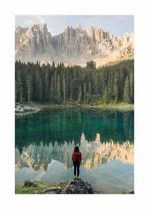 Persona con zaino accanto a un lago di montagna calmo, con foresta e pareti rocciose chiare