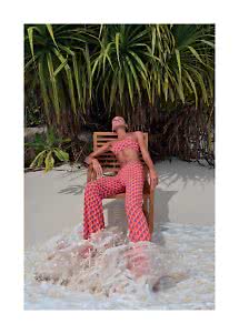 Woman in patterned bandeau top and pants sits on a chair on the beach with waves at her feet