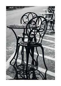 Black café table with two ornate metal chairs on a wet street