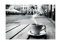 Steaming coffee cup on saucer with spoon on a wooden table at an outdoor café, black and white
