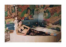 Model in schwarzer Spitzenwäsche und blauen Absatzschuhen an einer Badewanne vor bunter Mosaikwand