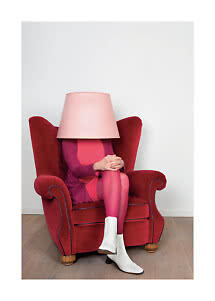 Personne en tenue rose et bottines blanches assise dans un fauteuil rouge, abat-jour sur la tête