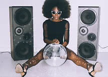 Donna con afro e occhiali da sole seduta tra due altoparlanti con una palla da disco