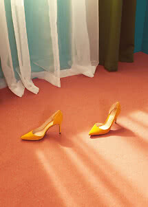 Pair of yellow high heels on a coral floor in front of sheer curtains.