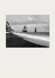 Foto in bianco e nero di una spiaggia di sabbia nera con faraglioni e onde sotto cielo nuvoloso
