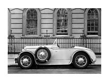 Photo en noir et blanc d’un cabriolet vintage garé devant un bâtiment aux fenêtres cintrées