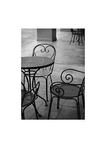 Foto en blanco y negro de mesa y sillas de hierro forjado en un patio con baldosas