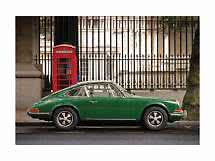 Green classic sports car parked beside a red telephone box on a city street