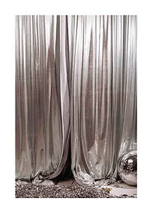 Photograph of silver lamé curtains in heavy vertical folds, a mirror ball resting against the fabric and foil confetti across the floor