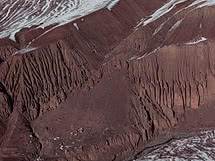 Ladera montañosa rojo óxido del Himalaya con finos surcos de erosión y delgadas vetas de nieve en las crestas
