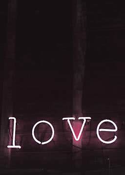 Pink neon sign reading "love" on a dark wooden wall